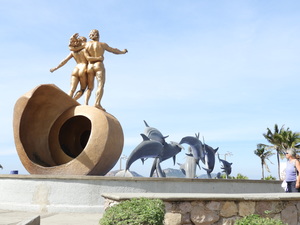 Sculpture of two humans striding along behind pod of leaping dolphins